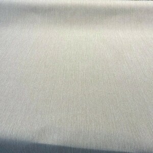Puede incluir: Primer plano de una tela beige con un sutil patr&oacute;n de espiga blanca. La tela tiene una textura lisa y una superficie ligeramente texturizada.