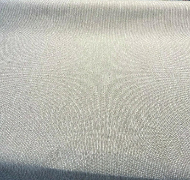 Puede incluir: Primer plano de una tela beige con un sutil patr&oacute;n de espiga blanca. La tela tiene una textura lisa y una superficie ligeramente texturizada.