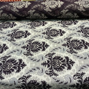 May include: A close-up of a fabric with a white background and a black damask pattern. The fabric is rolled up in the background.