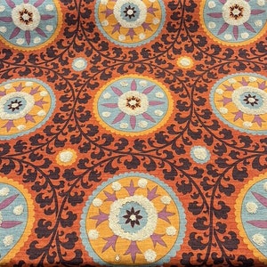 May include: A repeating pattern of orange, blue, and white floral medallions on a brown background. The fabric has a textured, embroidered look.