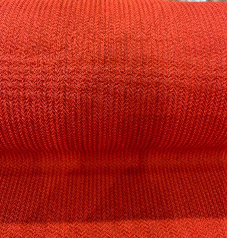 May include: Close-up of a red fabric with a herringbone weave pattern.