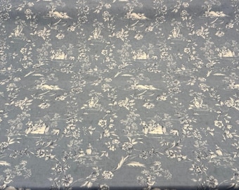 May include: Blue fabric with a repeating pattern of white floral and pastoral scenes. The design includes flowers, trees, and figures in a classic toile de Jouy style. The fabric has a soft, matte finish.