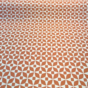May include: A white fabric with a repeating geometric pattern of orange diamonds and stars.