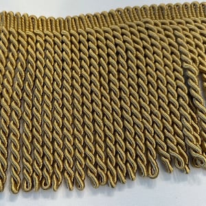 May include: Gold braided trim with a fringe. The trim is made of a soft, woven material and has a subtle sheen.