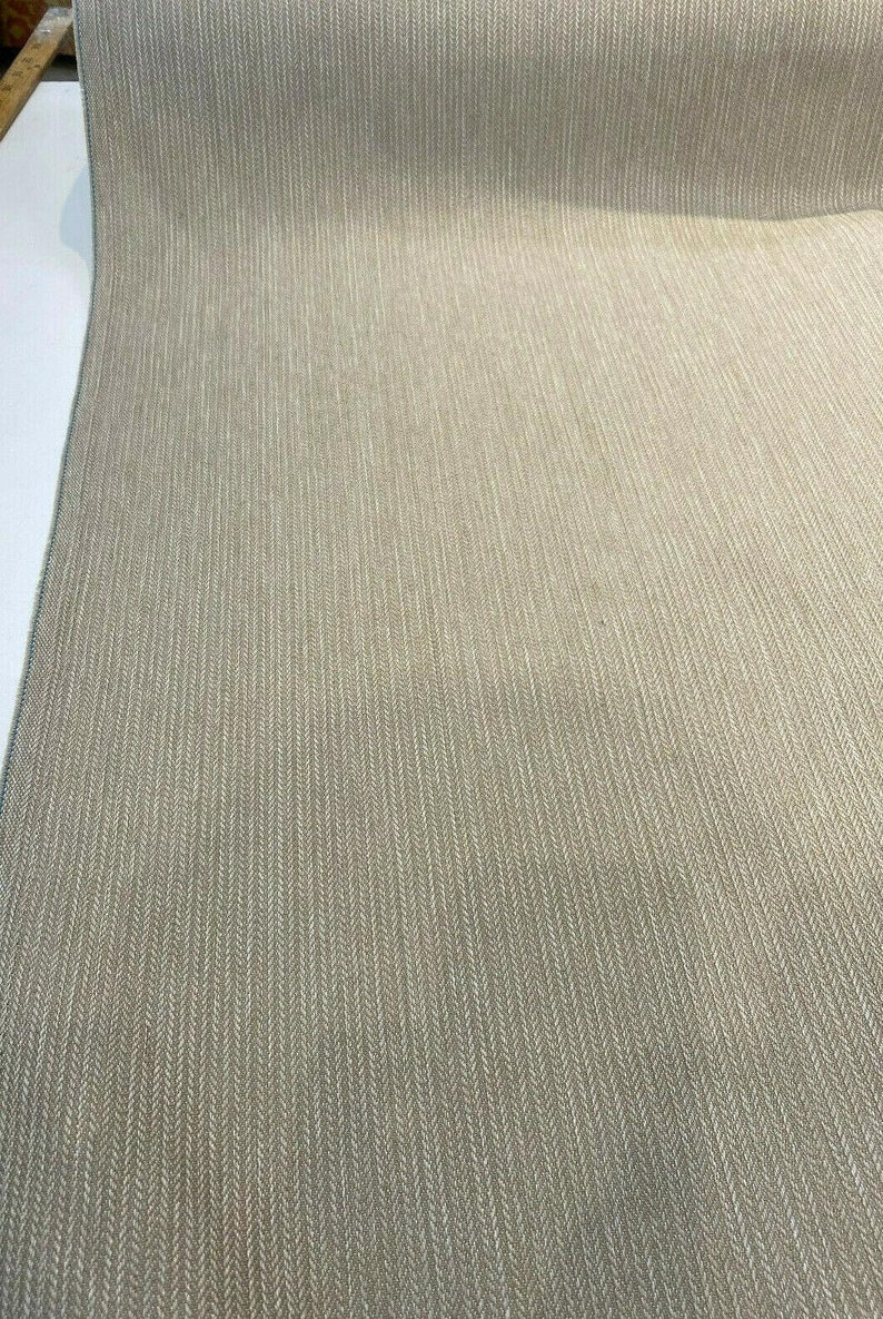 Puede incluir: Primer plano de una tela beige con un sutil patr&oacute;n de espiga. La tela tiene una textura suave y un acabado ligeramente brillante.