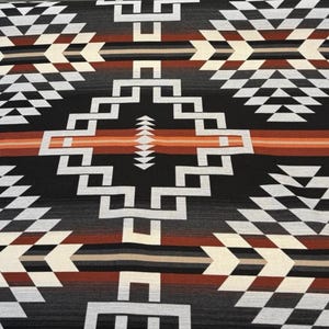 Puede incluir: Un textil con un patrón geométrico en negro, blanco, gris y tonos de marrón y naranja. El diseño presenta formas de diamante y escalonadas, creando una estética del suroeste o nativa americana.