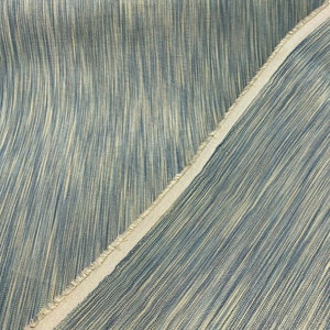 May include: Close-up of a blue and beige striped fabric with a raw edge. The fabric has a subtle sheen and a soft texture.
