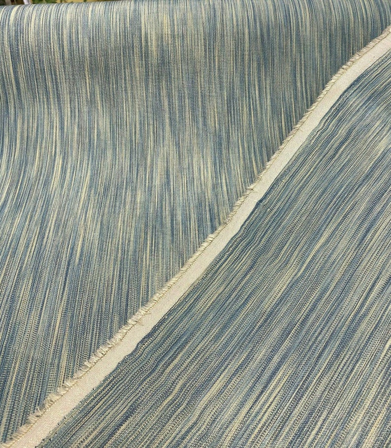 May include: Close-up of a blue and beige striped fabric with a raw edge. The fabric has a subtle sheen and a soft texture.