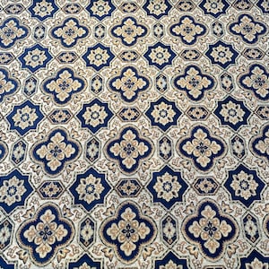May include: A close-up of a patterned carpet with a repeating design of blue, gold, and white. The pattern features a central four-leaf clover shape surrounded by smaller geometric shapes.