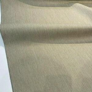 Puede incluir: Primer plano de una tela beige con un sutil patr&oacute;n de espiga. La tela tiene un tacto suave y texturizado, ideal para tapicer&iacute;a o cortinas.
