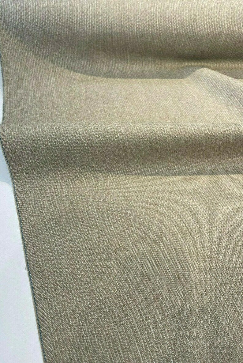 Puede incluir: Primer plano de una tela beige con un sutil patr&oacute;n de espiga. La tela tiene un tacto suave y texturizado, ideal para tapicer&iacute;a o cortinas.