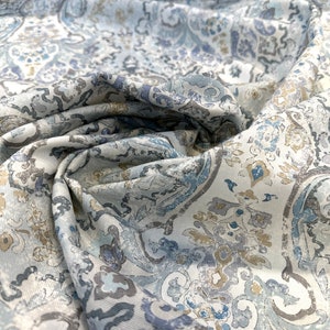 May include: A white fabric with a blue and brown paisley pattern. The fabric is folded and textured.