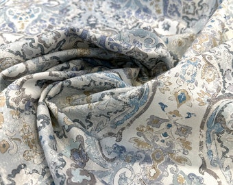 May include: A white fabric with a blue and brown paisley pattern. The fabric is folded and textured.