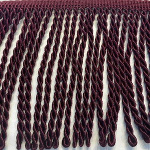 May include: Burgundy twisted fringe trim. The fringe is made of a soft, silky material and has a subtle sheen. The fringe is approximately 1 inch in length.