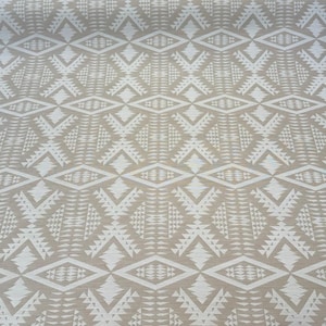May include: Tan and white geometric patterned fabric. The design features repeating diamond and triangular shapes. The fabric has a textured appearance and is suitable for various craft projects or home decor.