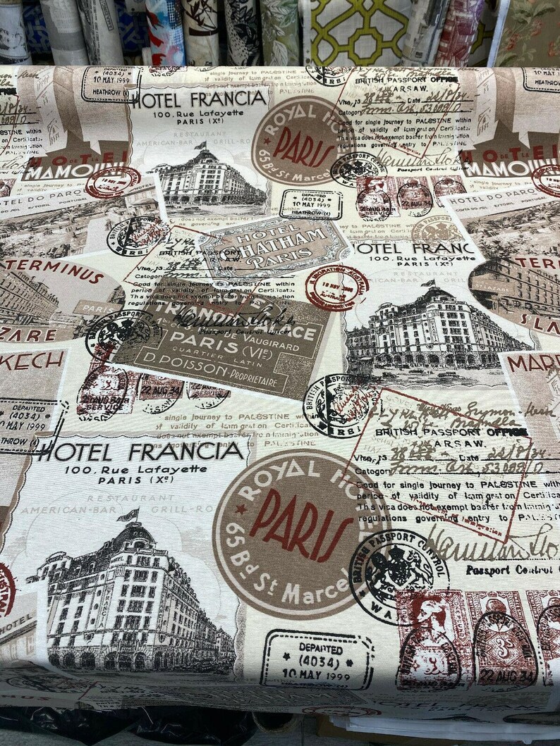 May include: A beige fabric with a vintage travel theme. The fabric features a repeating pattern of stamps, hotel logos, and travel-related text. The text includes "Hotel Francia", "Royal Hotel Paris", and "British Passport Office".
