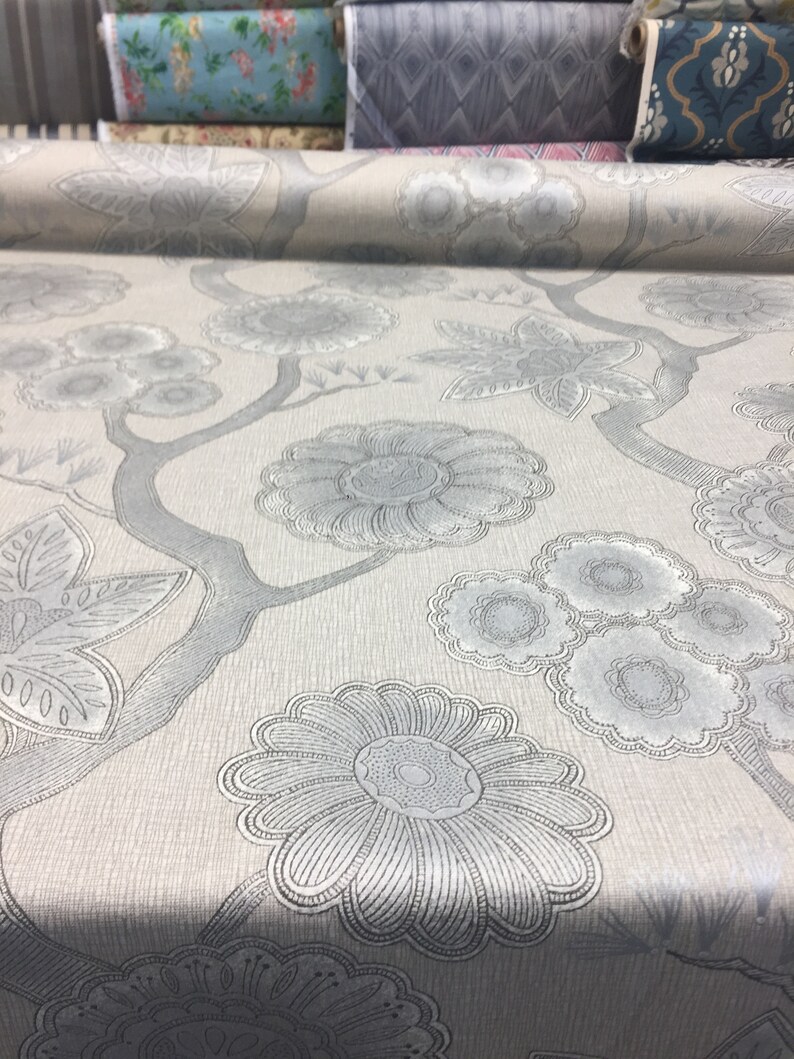 Puede incluir: Primer plano de una tela gris claro con un patr&oacute;n floral plateado. La tela tiene una textura sutil y un dise&ntilde;o delicado.