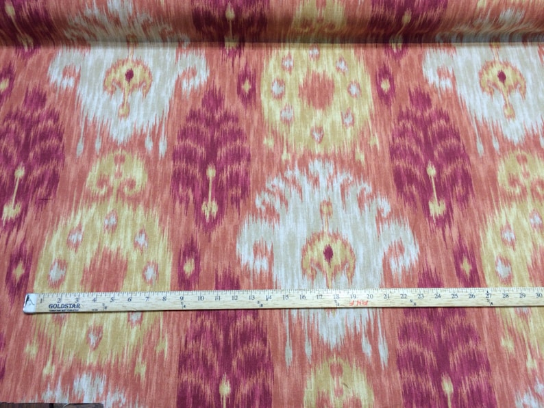 May include: Red, beige, and yellow ikat fabric with a repeating pattern. The fabric is measured with a ruler, showing 30 inches.