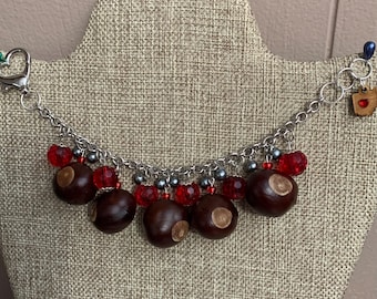 May include: A silver chain necklace with red and silver beads and brown buckeye nuts. The necklace has a silver clasp and a small charm with a red heart.