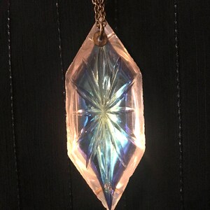 May include: A clear iridescent glass pendant shaped like a diamond with a starburst pattern hangs from a gold chain.
