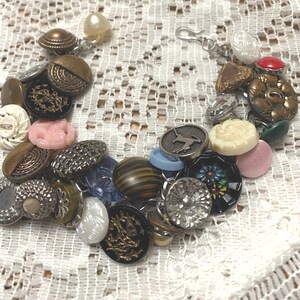 May include: A bracelet made of a variety of vintage buttons in different colors, shapes, and sizes. The buttons are attached to a silver chain with a clasp.