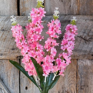 May include: A bouquet of pink artificial flowers with white centers. The flowers are arranged in a cluster and have a green stem.