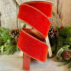 May include: A spool of bright red velvet ribbon with a gold edge. The ribbon is rolled up and sitting on a wooden surface.