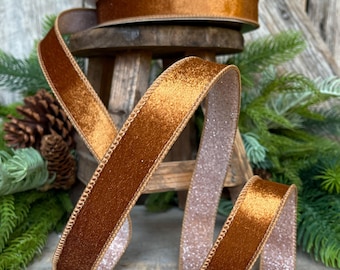 May include: A spool of metallic copper-colored ribbon with a smooth, reflective finish on one side and a textured, glittery silver-toned backing. The ribbon features stitched edges and is displayed in a coiled, flowing arrangement.