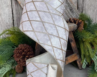 May include: A roll of wide, off-white ribbon with a velvet texture and a gold diamond pattern. The ribbon has a satin backing and a brown spool. Perfect for holiday or craft projects.