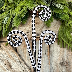 May include: Decorative black and white checkered fern stems with curled ends. The stems are set against a backdrop of green pine branches and a rustic wooden door. The fern stems add a touch of whimsy to any home decor.