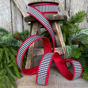 May include: A spool of black and white checkered ribbon with a red border sits atop a small wooden stool. The ribbon is unraveled, displaying its red underside. Greenery and a wooden background complete the scene.