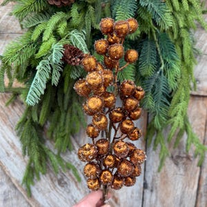 May include: A decorative floral pick featuring a cluster of round, copper-colored berries with a textured, glittery finish. The berries are attached to a central stem, creating a dense, vertical arrangement of metallic spheres.