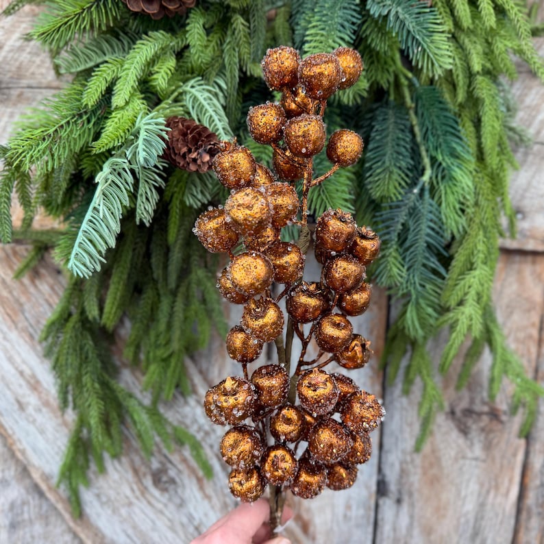 May include: A decorative floral pick featuring a cluster of round, copper-colored berries with a textured, glittery finish. The berries are attached to a central stem, creating a dense, vertical arrangement of metallic spheres.