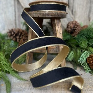 May include: Black velvet ribbon with a gold trim. The ribbon is rolled up on a wooden stool and is surrounded by pine branches.