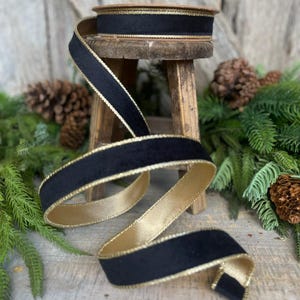 May include: Black velvet ribbon with a gold trim. The ribbon is coiled on a wooden stool.