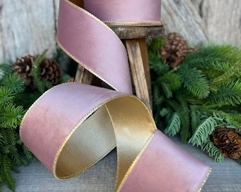 May include: A spool of dusty rose ribbon with a smooth, satin-like finish on one side and a metallic gold underside. The edges of the ribbon are finished with a thin, gold-colored stitched trim that runs along both sides of the entire length.