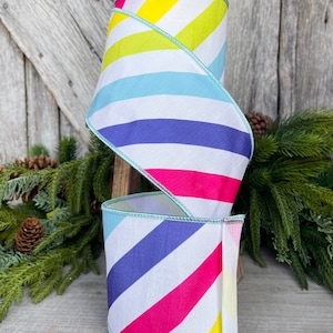 May include: A roll of white ribbon with diagonal stripes in yellow, light blue, purple, and pink. The ribbon has a light blue edge.