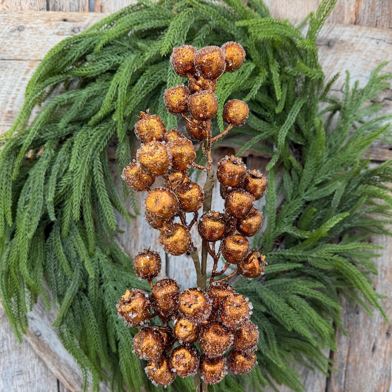 May include: A decorative floral stem featuring numerous round, copper-colored berries with a textured, glittery finish. The berries are clustered along a central brown branch, creating a dense, spherical arrangement that mimics natural fruit.