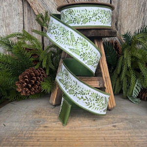May include: A spool of white ribbon featuring a repeating green fern leaf pattern. The ribbon has a solid green edge and is draped in a spiral shape, showcasing the botanical print against the white fabric background with a finished texture.
