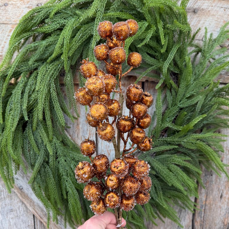 May include: A decorative floral stem featuring numerous round, copper-colored berries with a textured, glittery finish. The berries are clustered along thin, brown branches, creating a dense, spherical arrangement on a single vertical stem.