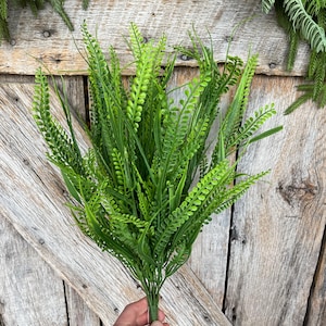 May include: A bundle of vibrant green artificial fern stems. The faux foliage features a mix of textures, with long, slender leaves and delicate, rounded fronds. The stems are held together at the base, creating a full, natural look, perfect for home decor.