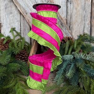 May include: A spool of decorative ribbon featuring alternating horizontal stripes of bright fuchsia pink and lime green. The ribbon has ruffled edges along both sides, creating a textured, wavy appearance as it wraps around the central spool.