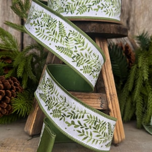 May include: A roll of white wired ribbon featuring a repeating green fern leaf pattern. The ribbon has solid green finished edges and is coiled in a spiral shape, displaying the botanical print clearly against the white fabric background.