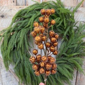 May include: A decorative floral stem featuring numerous round, copper-colored berries with a textured, glittery finish. The berries are clustered along a thin, brown branch, creating a dense, spherical arrangement of metallic-toned fruit.