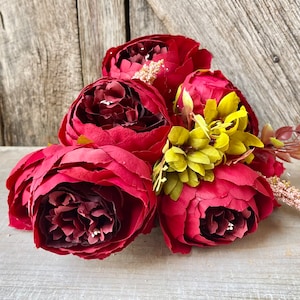 May include: A bouquet of deep red peonies with yellow accents. The flowers are arranged in a cluster and have a soft, velvety texture.