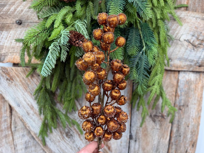 May include: A decorative floral stem featuring numerous round, copper-colored berries with a textured, glittery finish. The berries are clustered along thin, brown branches, creating a dense, spherical arrangement on the main stem.