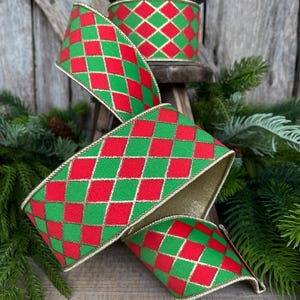 May include: A spool of decorative ribbon with a red and green diamond pattern. The ribbon has gold trim and is displayed with evergreen branches in the background. The ribbon is suitable for holiday and craft projects.