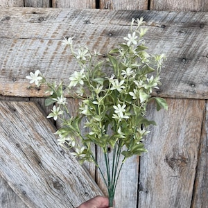 May include: A bouquet of artificial white flowers with green leaves. The flowers have a delicate, star-shaped appearance.