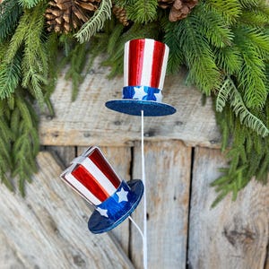 May include: Two red, white, and blue Uncle Sam top hat picks. The hats are made of paper and have a glitter finish. The picks are perfect for adding a patriotic touch to your home decor.