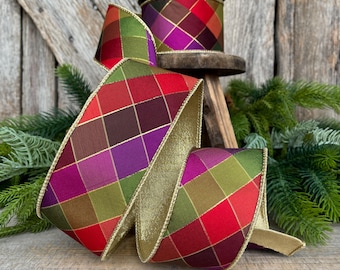 May include: A colorful, decorative ribbon with a harlequin pattern in red, green, purple, and brown. The ribbon has gold trim and is displayed on a wooden surface with greenery in the background. A spool of the same ribbon sits on a small wooden stool.